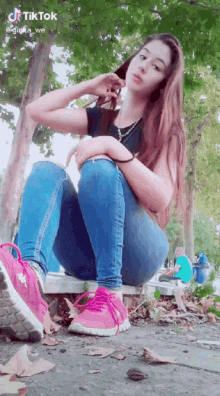 a girl wearing blue jeans and pink shoes is sitting on a bench