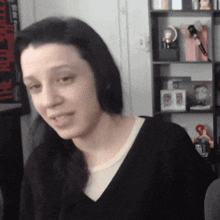a woman in a black shirt is sitting in front of a shelf with a clock on it