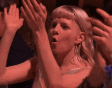 a woman with blonde hair is clapping her hands in a crowd .