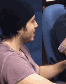 a man wearing a beanie and a purple shirt is sitting in a blue chair .