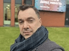 a man wearing a scarf is standing in front of a large billboard .