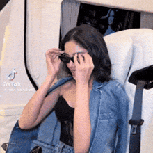 a woman wearing sunglasses and a denim jacket is sitting in a car seat .