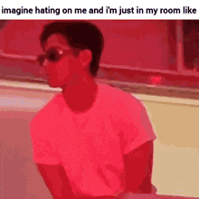 a man wearing sunglasses and a pink shirt is sitting in a room with a red background .