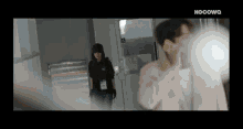 a man is talking on a cell phone while a woman stands behind him in a hallway .