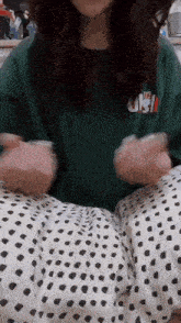 a woman wearing a green t-shirt and polka dot pants is sitting on a bed .