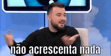 a man with a beard is sitting in front of a television with the words " não acrescenta nada " on the screen behind him