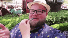 a man with a beard wearing glasses and a hat is eating something