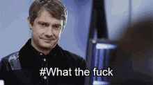 a man in a black shirt is smiling and says # what the fuck