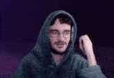 a man with a beard and glasses is wearing a hoodie and holding his fist up .