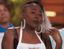 a woman wearing hoop earrings and an apron with the name shelly on it