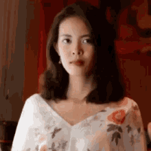 a woman is wearing a white floral top and making a funny face .