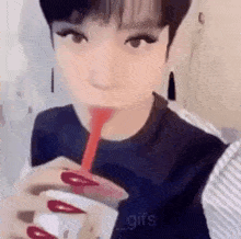 a girl with long red nails is drinking from a cup with a straw .
