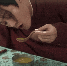 a man in a red jacket is eating soup with a spoon