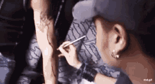 a man is drawing a tattoo on another man 's arm with a marker .