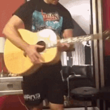 a man is playing an acoustic guitar in front of a red wall