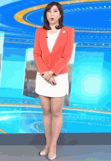 a woman in a red jacket and white skirt is standing on a stage