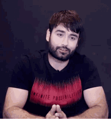 a man with a beard wearing a red t-shirt that says infinite possibilities .