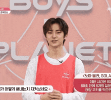 a young man stands in front of a sign that says " boys planet "