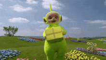a teletubbies character is holding a yellow box in a field of flowers