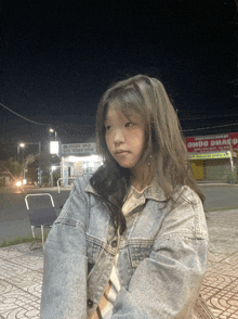 a girl in a denim jacket stands in front of a red sign that says ' saigon ' on it
