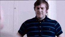 a man wearing a blue and black striped shirt is standing in front of a white wall .