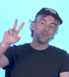 a man wearing a hat that says billboard on it is giving the peace sign