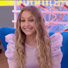 a woman with long blonde hair is smiling and wearing a purple shirt with puffed sleeves