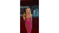 a woman in a pink dress is standing on a red carpet holding a gold trophy .