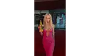 a woman in a pink dress is standing on a red carpet holding a gold trophy .