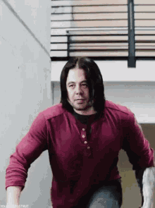 a man with long hair and a red shirt is standing on a set of stairs .