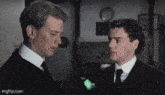 two men in suits and ties are standing next to each other looking at each other .