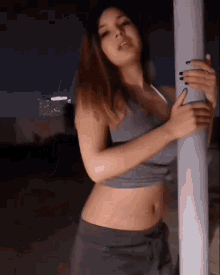 a woman in a crop top and shorts is leaning against a pole at night .