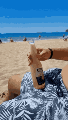 a person on the beach holding a bottle of corona beer