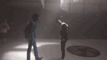 two men are standing next to each other in a dark room and talking to each other .