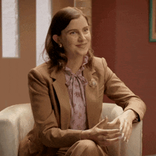 a woman sitting in a chair wearing a brown suit and a brooch with a cross on it