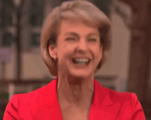 a woman wearing a red jacket is laughing with her eyes closed