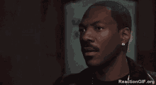a man with a mustache and earrings is talking on a cell phone in a dark room .