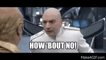 a bald man in a white suit is talking to another bald man in a room .