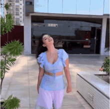 a woman in a blue top and pink pants is standing on a patio .