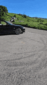 a black car is parked in a parking lot with a field in the background