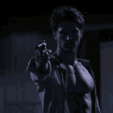 a shirtless man pointing a gun at the camera