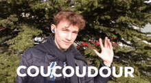 a young man is waving in front of a tree with the word coucoudour written on the bottom