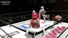 a woman in a stardom wrestling ring holds up a championship belt