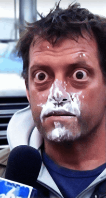 a man with whipped cream on his face is talking into a microphone with the word news on it