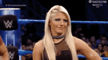 a blonde woman is standing in a wrestling ring with a choker around her neck .