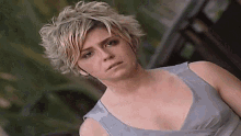 a woman with short blonde hair is wearing a grey dress and looking at the camera .