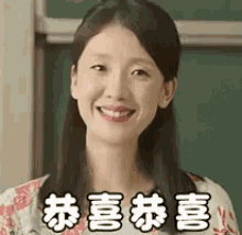 a woman is smiling in front of a blackboard in a classroom while wearing a floral dress .