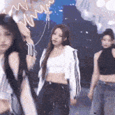 a woman in a white crop top and black pants is dancing on a stage with other women .