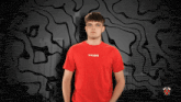 a man wearing a red tribe t-shirt stands with his hands in his pockets