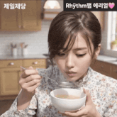 a woman is holding a bowl of soup with a spoon in her hand with rhythm written on the bottom
